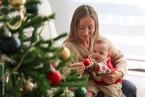 Mom and her newborn decorating a Christmas tree together. Copy space, background.