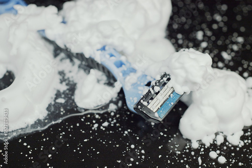 Close-up of a disposable razor on a wet black surface with shaving foam.