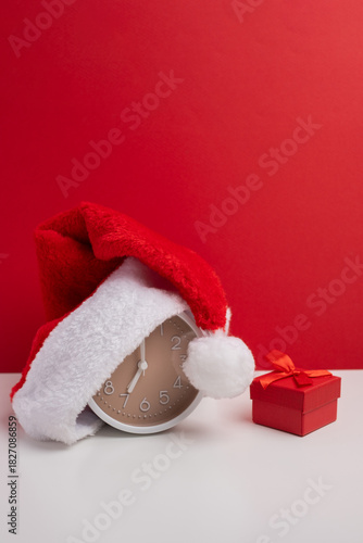 Santa hat, alarm clock, and gift box on vivid red background. Christmas Countdown.