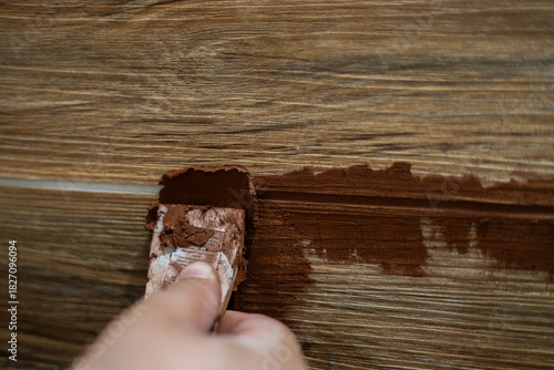 Applying brown grout by hand with a trowel to fill narrow joints between wood-look ceramic tiles during a renovation. Close-up of the wall renovation and finishing work.