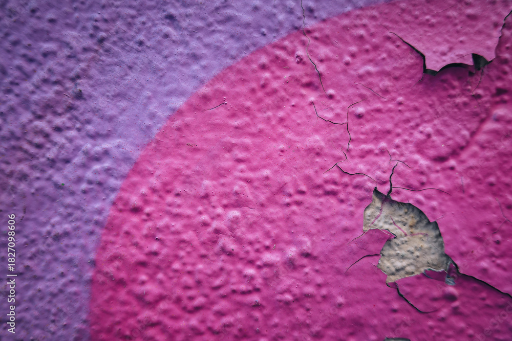 Obraz premium Close-up view of textured building wall with peeling paint. The surface features vibrant pink and purple colors, revealing a rough, damaged area underneath.