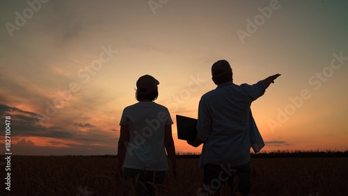 Farmers business people grow grain. Farmers partners with computer evaluates wheat sprouts in field. Farmers man and woman working in wheat field with laptop in agriculture. Silhouette. Organic wheat