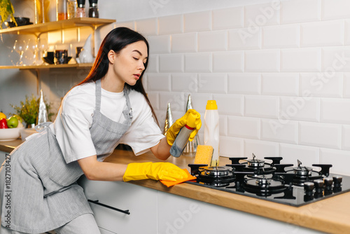 Woman cleaning gas stove with spray cleaner