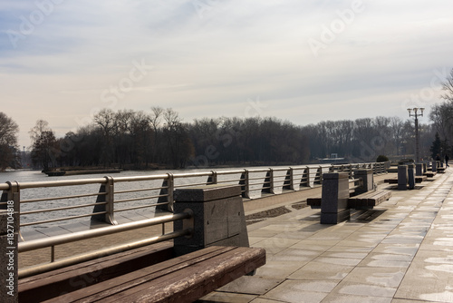 Empty riverside promenade with benches and metal railing at sunset