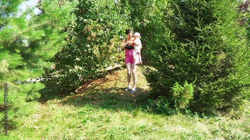A mother walks with her baby in a beautiful garden filled with vibrant trees and soft grass