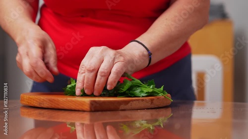 Hands skillfully chop fresh herbs on a wooden board.