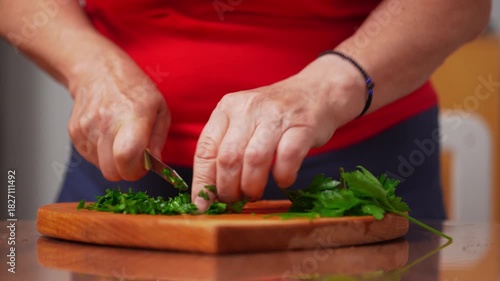 Hands skillfully chop fresh herbs on a wooden board.