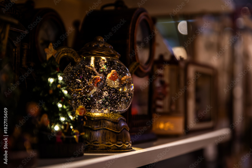 Naklejka premium Illuminated snow globe with birds and glitter inside on a shelf, wonder and cozy decoration for Christmas.