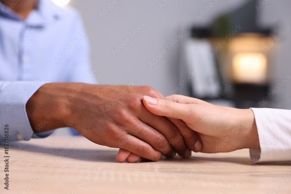 Obraz premium African-american man holding hands with woman at wooden table indoors, closeup