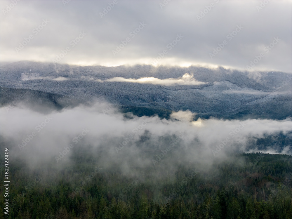 Obraz premium Snowy Mountain Range Above Forest Clouds in BC, Canada — Misty Winter Morning Panorama View