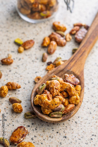 Nuts coated in sugar glaze on wooden spoon on kitchen table.