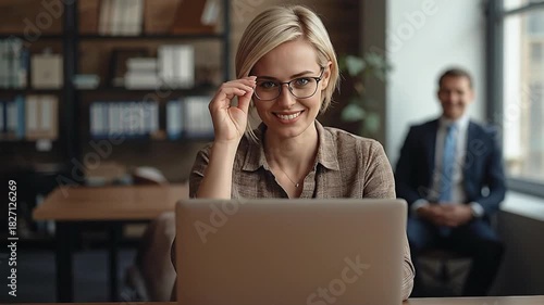 Smiling Professional Woman in Glasses Adjusting Eyewear, Working on Laptop in a Modern Office Environment
