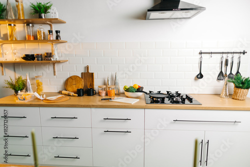 Modern white kitchen interior with wooden countertop, stove and shelves, clean home cooking background with copy space.