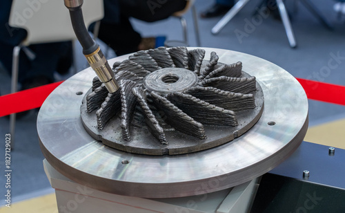 Fototapeta Naklejka Na Ścianę i Meble -  Robotic arm using advanced metal additive manufacturing to precisely build complex, textured turbine-like component on circular platform, highlighting industrial 3D printing technology