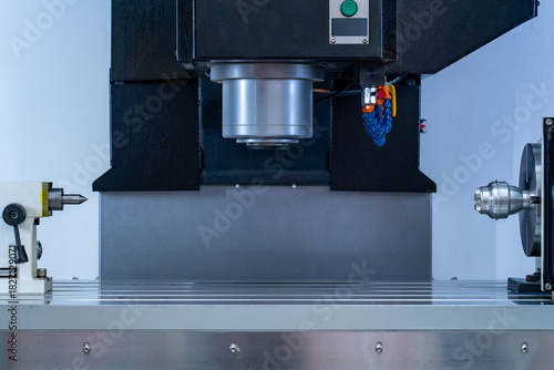 Close-up of modern industrial CNC precision machining equipment showing spindle, work holding devices, and slotted table in manufacturing workshop environment