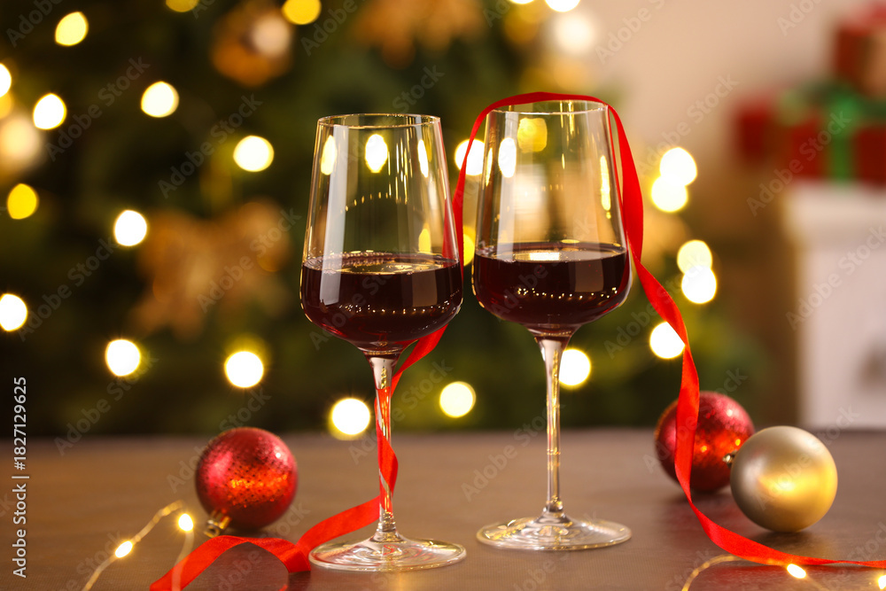 Fototapeta premium Glasses of red wine and Christmas decor on wooden table against background with blurred lights