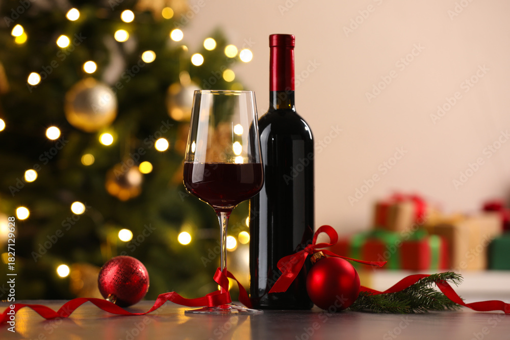 Fototapeta premium Glass of red wine, bottle and Christmas decor on wooden table against background with blurred lights