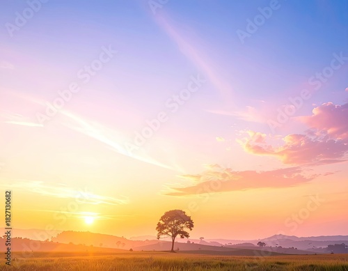 Majestic sunset over a tree in a golden field, mountains, and colorful sky
