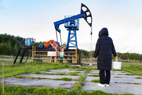 Worker performs maintenance, Technician checks machinery outdoors, Field staff inspects oil extraction device, Laborer surveys industrial equipment amidst cloudy environment