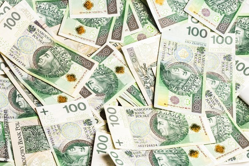 A vibrant spread of Polish 100-zloty banknotes arranged in a scattered pattern, showcasing detailed security elements, rich green tones, and historical portrait artwork on display.