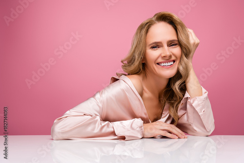 Smiling mature woman with blonde hair in pink outfit posing on a gentle pink background
