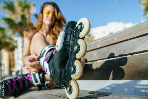 Woman tying roller skates laces on bench in urban setting