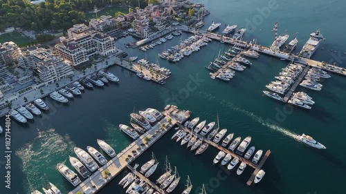 Porto Montenegro luxury marina aerial 4K drone shot at golden hour, with rows of white yachts and sailboats moored along geometric piers in calm blue water at Tivat waterfront.