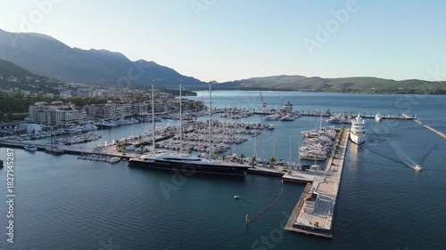 Porto Montenegro luxury marina sunrise aerial 4K drone view with calm blue water, soft morning light, and rows of white yachts and sailboats moored along piers at Tivat waterfront.