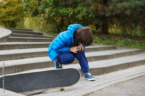 Little boy suffering from knee pain on stairs after fall from skateboard outdoors. Child in danger