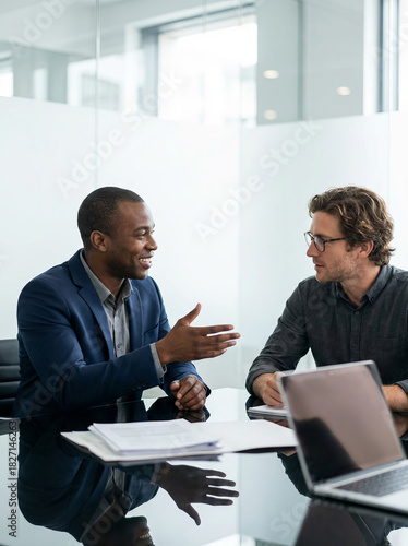 Business collaboration and partnership with two diverse businessmen discussing a project in a modern office boardroom.