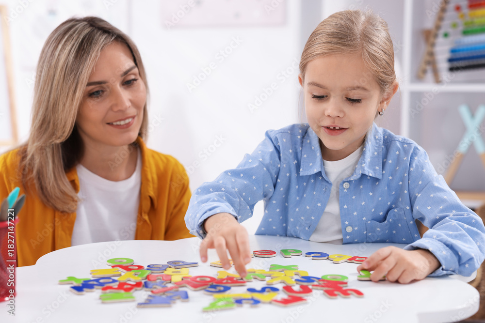 Fototapeta premium Mother teaching her daughter alphabet at white table indoors