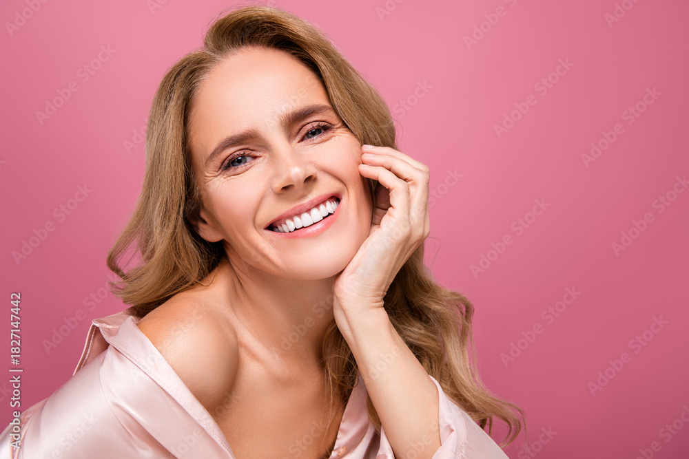 Fototapeta premium Beautiful mature woman with blonde hair smiling on a soft pink background in elegant sleepwear style