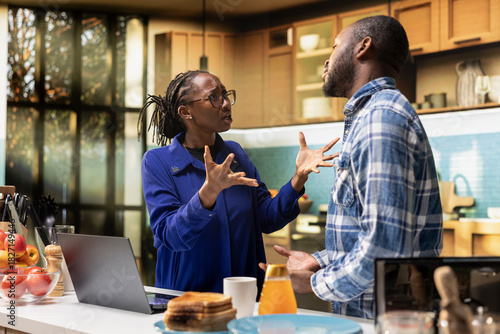 Upset African American couple fighting at home in their kitchen. Black woman looks offended and yelling at man, symbolizing emotional stress and difficulty of disagreement and argument.