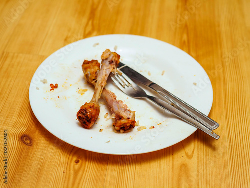 Dirty plate after meal with chicken drumstick bones and fork and knife. Finished dinner with meat.