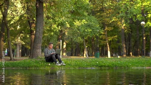 Young man working on laptop in riverside park, 4K