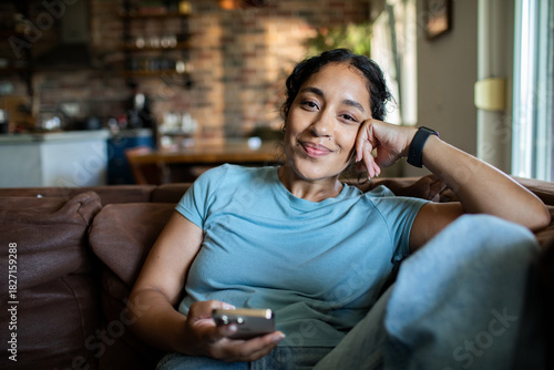 Young woman relaxing with smartphone at home, content