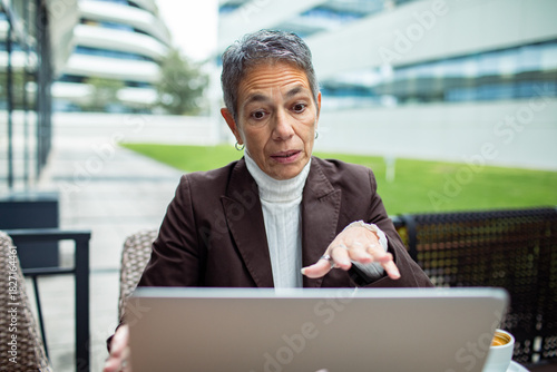Mature businesswoman looking concerned on laptop in office courtyard