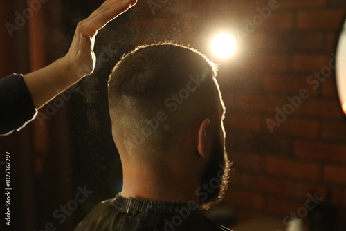 Hairstylist applying talcum powder onto man's hair at salon, closeup