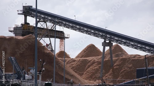 A large woodchip processing facility in Portland, Victoria, featuring conveyor belts transporting woodchips onto tall storage piles. Concept of industrial timber processing, bulk material handling