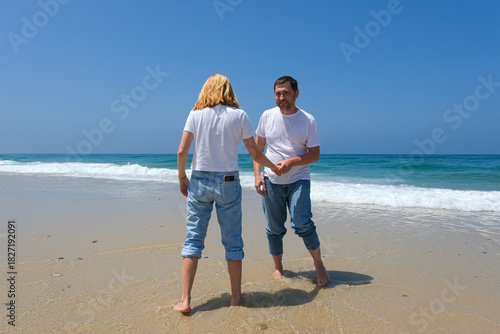 Joyful couple playing at the water's edge on a sunny beach, dressed in casual jeans and white tshirts
