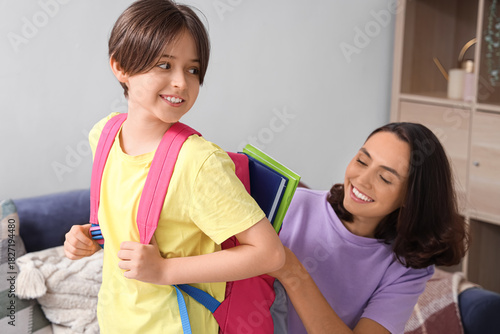 Mother helping her little son to pack schoolbag in living room