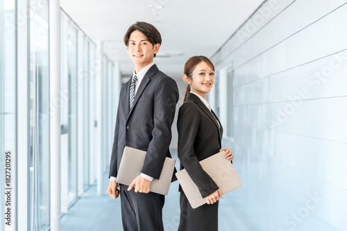 Young Asian businessmen and women in suits standing in an office corridor
