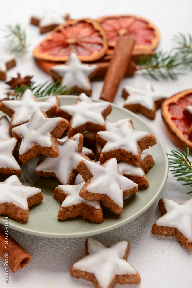Fototapeta premium Plate with delicious stars shaped Christmas cookies, orange dried pieces and fir tree branches on light background, closeup