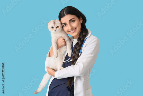 Young female veterinarian holding cute Scottish fold cat on blue background