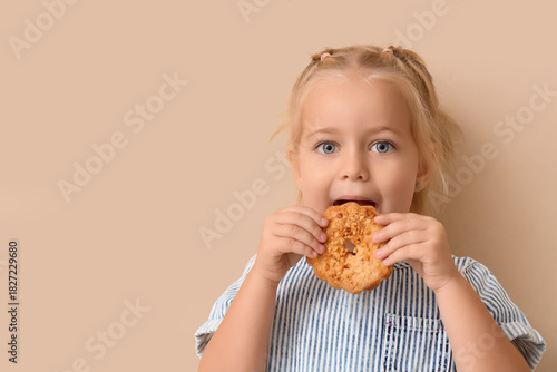 Foto Cute little girl eating tasty cookie on beige background