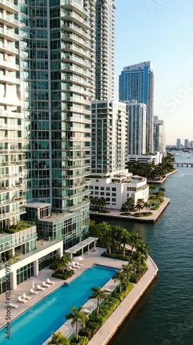 Modern waterfront high-rise buildings, pool, and palm trees beside a calm body of water