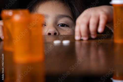 A close-up portrait shot showing the face of a young girl (preschooler) with innocence and curiosity as she is reaching for unattended prescription pills or bottles.