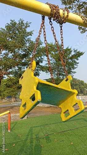 Colorful wooden swing with rusty chains hanging in an outdoor playground during sunny weather, capturing childhood nostalgia, play area equipment, and a calm park atmosphere.