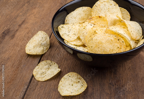Potato Chips with Herbs in a Black Bowl on Rustic Wooden Background