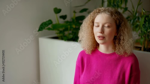 Young woman with curly hair in pink sweater indoors
